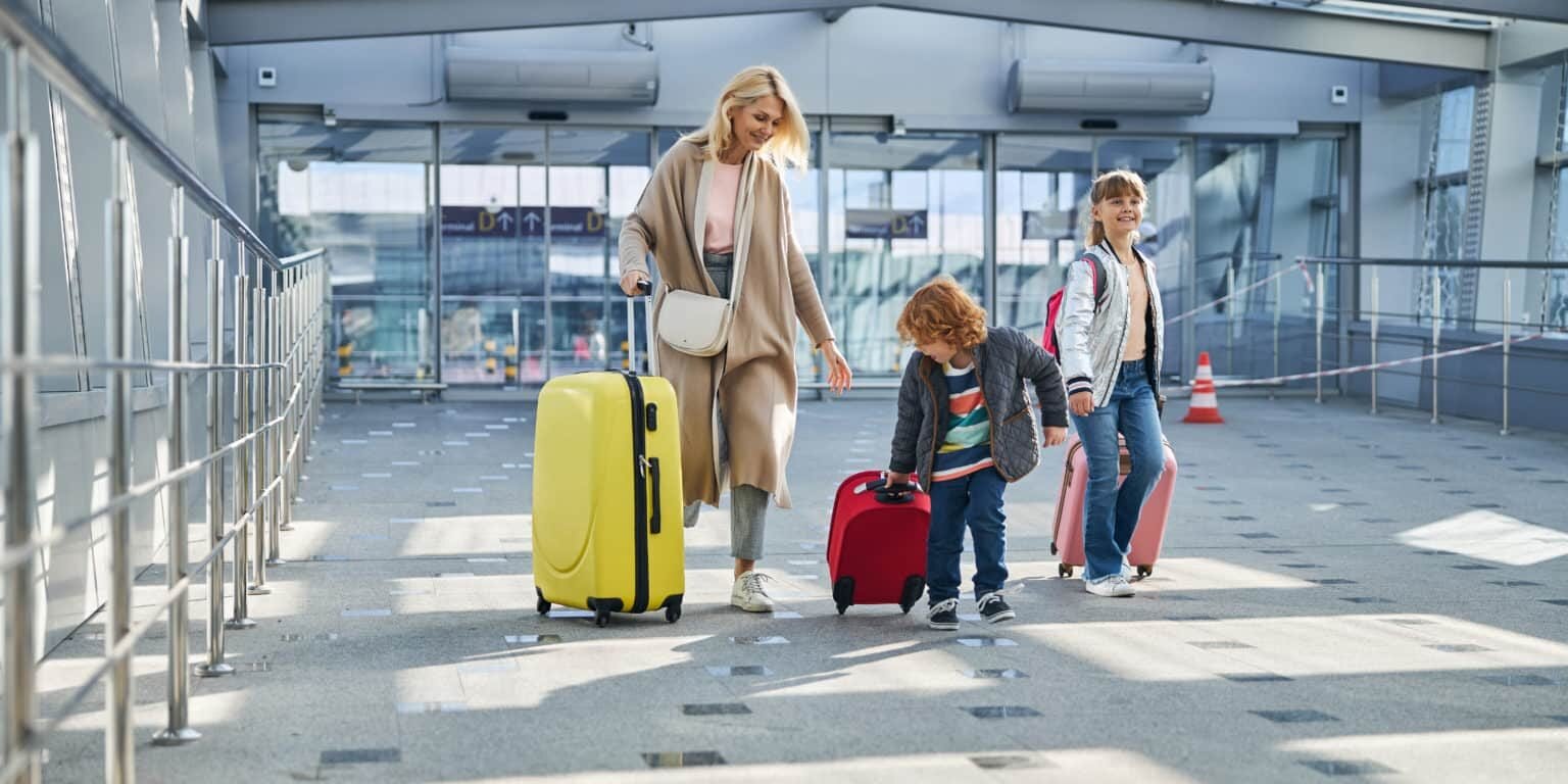 Lively siblings and their mother leading their colourful suitcases through the sunlit hallway of an airport